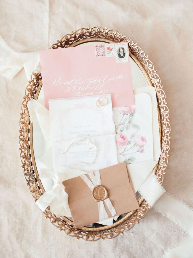Elegant bridal shower invitation suite with wax-sealed envelopes and romantic calligraphy displayed on an ornate gold tray.