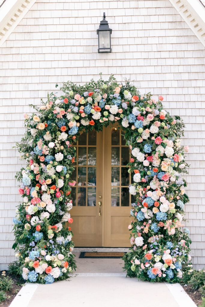 Colorful floral arch with roses, peonies, and hydrangeas in pastel tones framing chapel entrance – luxury wedding flowers Dallas TX